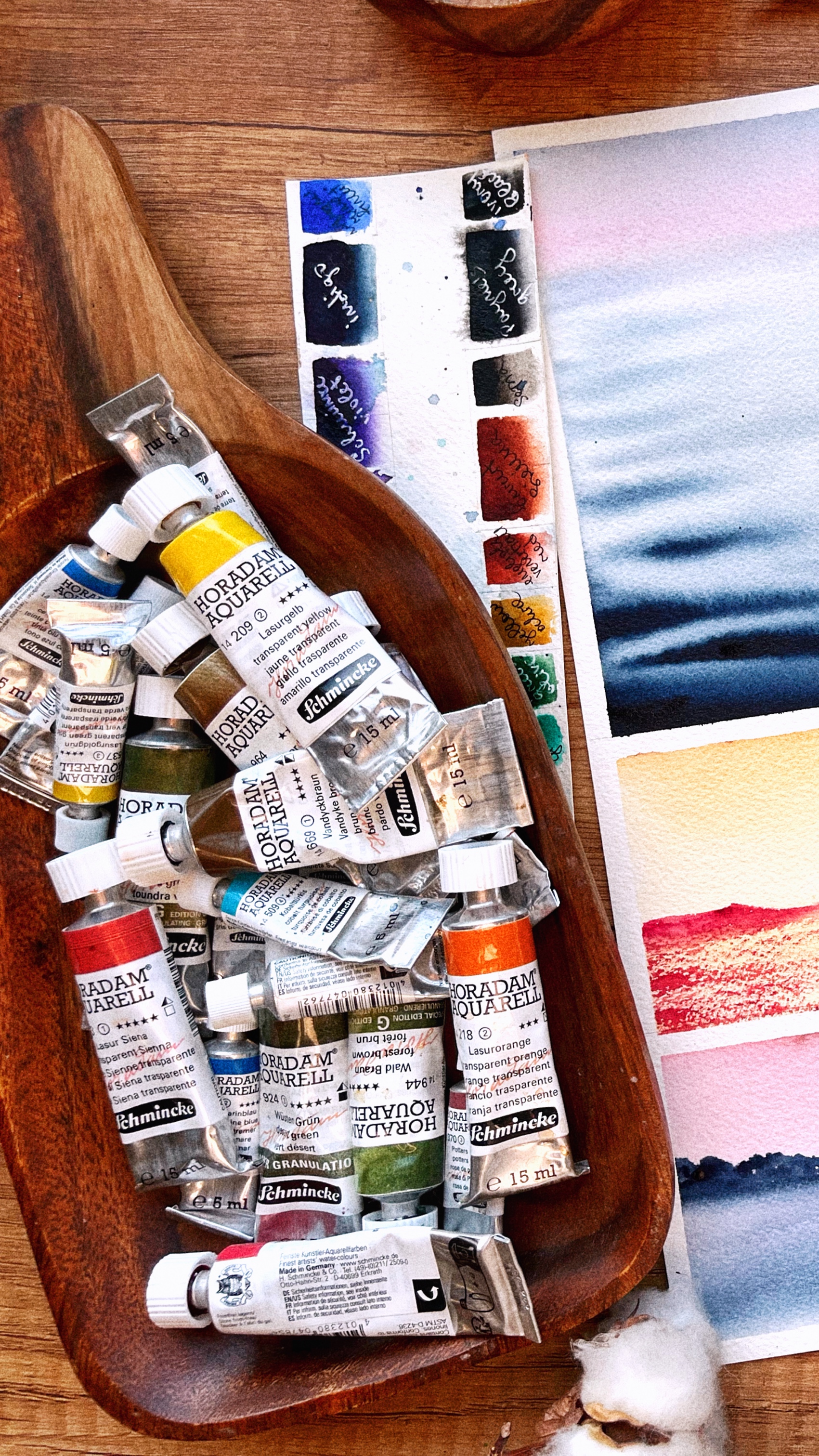 A wooden bowl filled with watercolor paint tubes